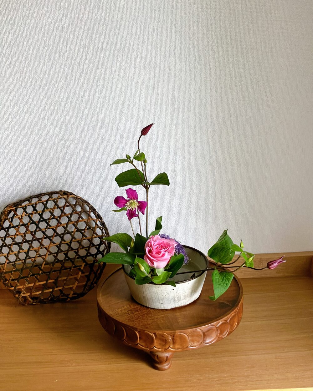 A minimal arrangement featuring a single rose and moving clematis stems set inside a deep, round Japanese ceramic plate.
