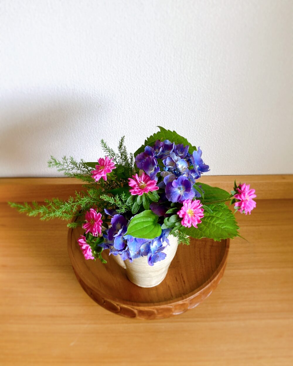 A top-down view of the hydrangea and aster arranged inside the ceramic pitcher.