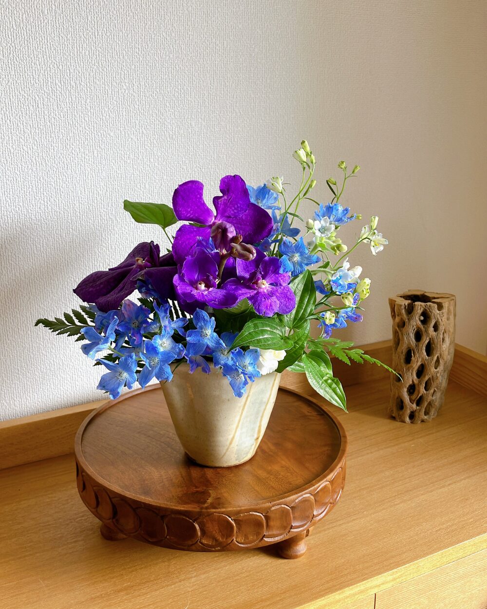 Close-up of a purple Vanda orchid styled with delicate blue Delphinium and small green leaves.