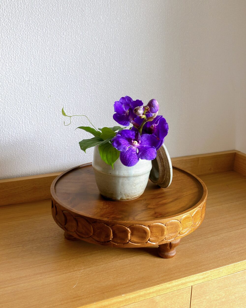 Close-up of a purple Vanda orchid styled naturally inside an old Japanese ceramic jar with a lid.