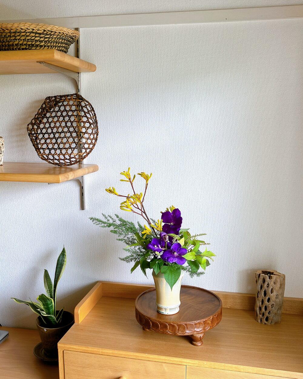 A Vanda orchid and Kangaroo Paw arrangement on a shelf next to a traditional Japanese bamboo basket.