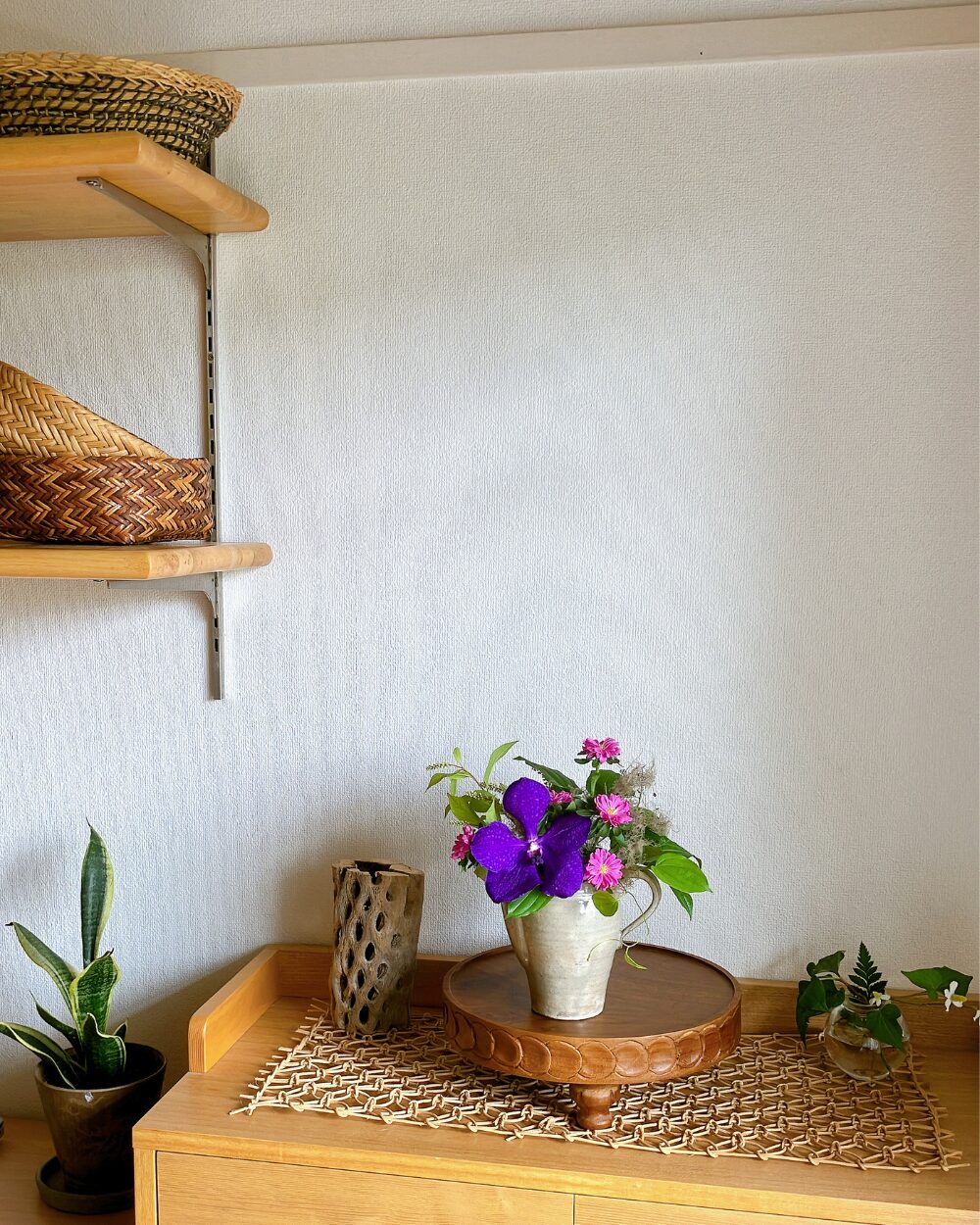 A Vanda orchid and pink Aster arrangement placed on a woven rattan sheet on a wooden shelf.