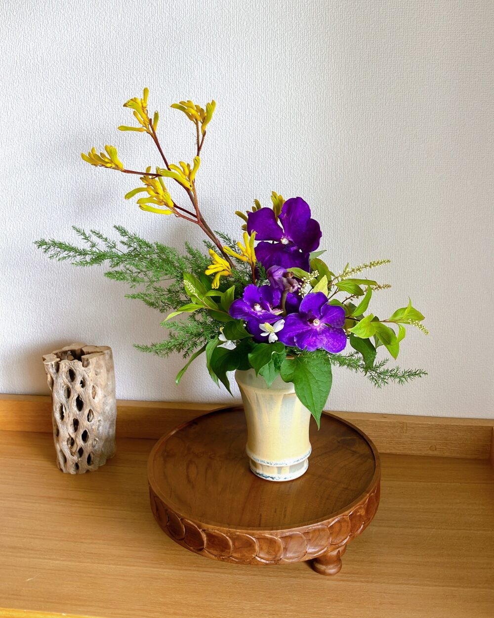 Close-up of a purple Vanda orchid and yellow Kangaroo Paw arrangement with rich green foliage.