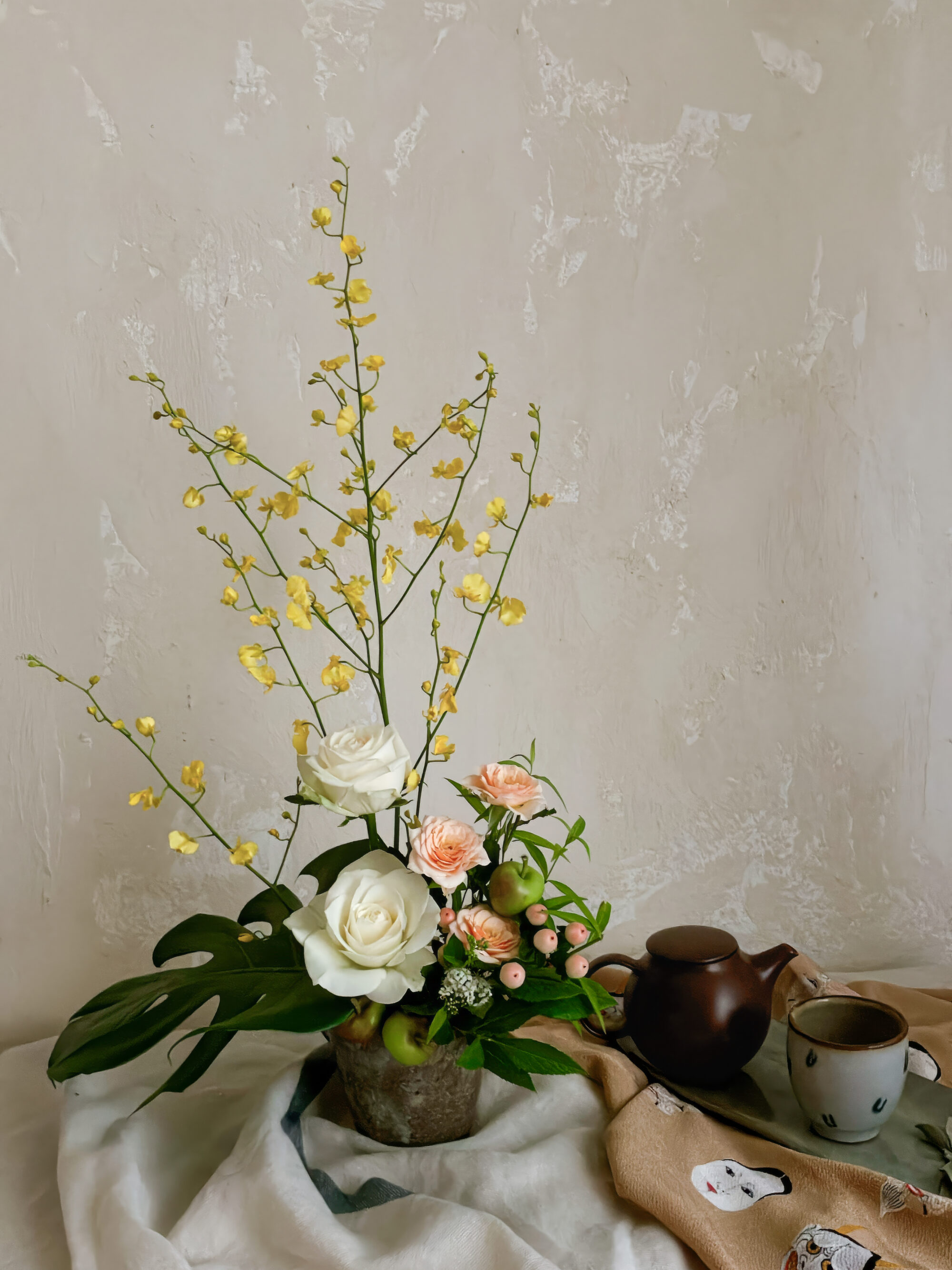 An art poster style photograph highlighting the vertical lines of yellow oncidium orchids and a white rose in a wide Japanese vessel, using a graphic composition.
