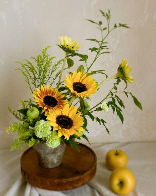 A fine-art photo preview of the flowing sunflower and green carnation arrangement isolated against a chic, dark moody backdrop.