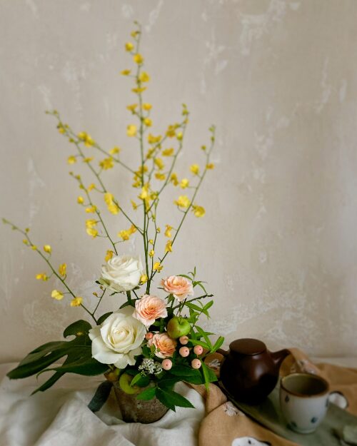 An art poster style photograph highlighting the vertical lines of yellow oncidium orchids and a white rose in a wide Japanese vessel, using a graphic composition.