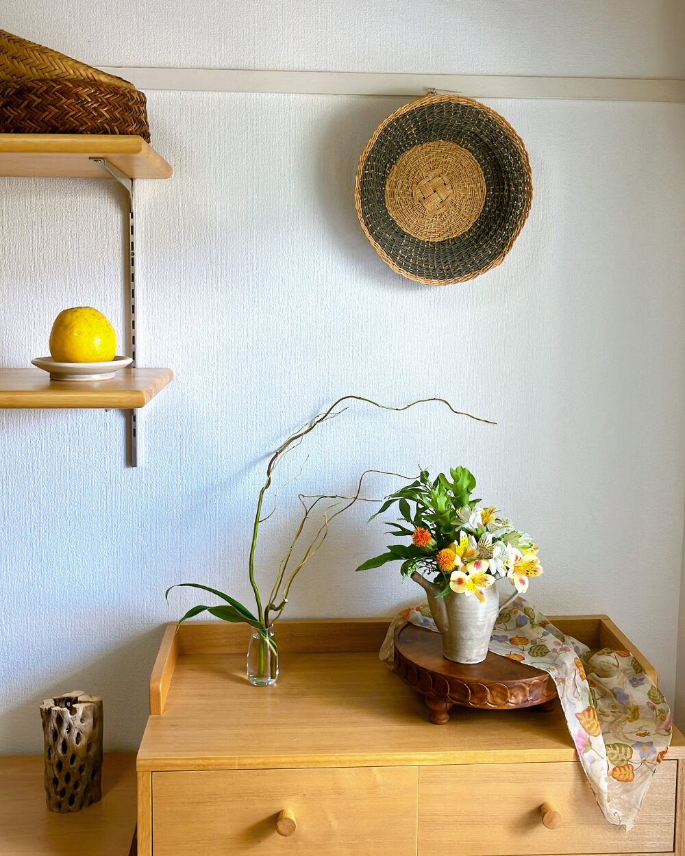 A shelf display with a pitcher arrangement, a basket, and a scarf.
