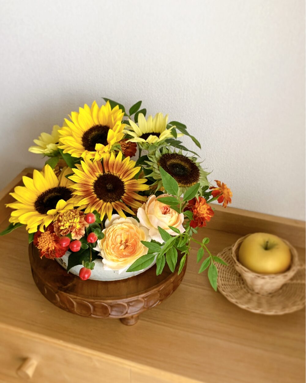 A detailed close-up of a sunflower with its petals removed, surrounded by field marigolds, roses, and summer berries in a low plate.