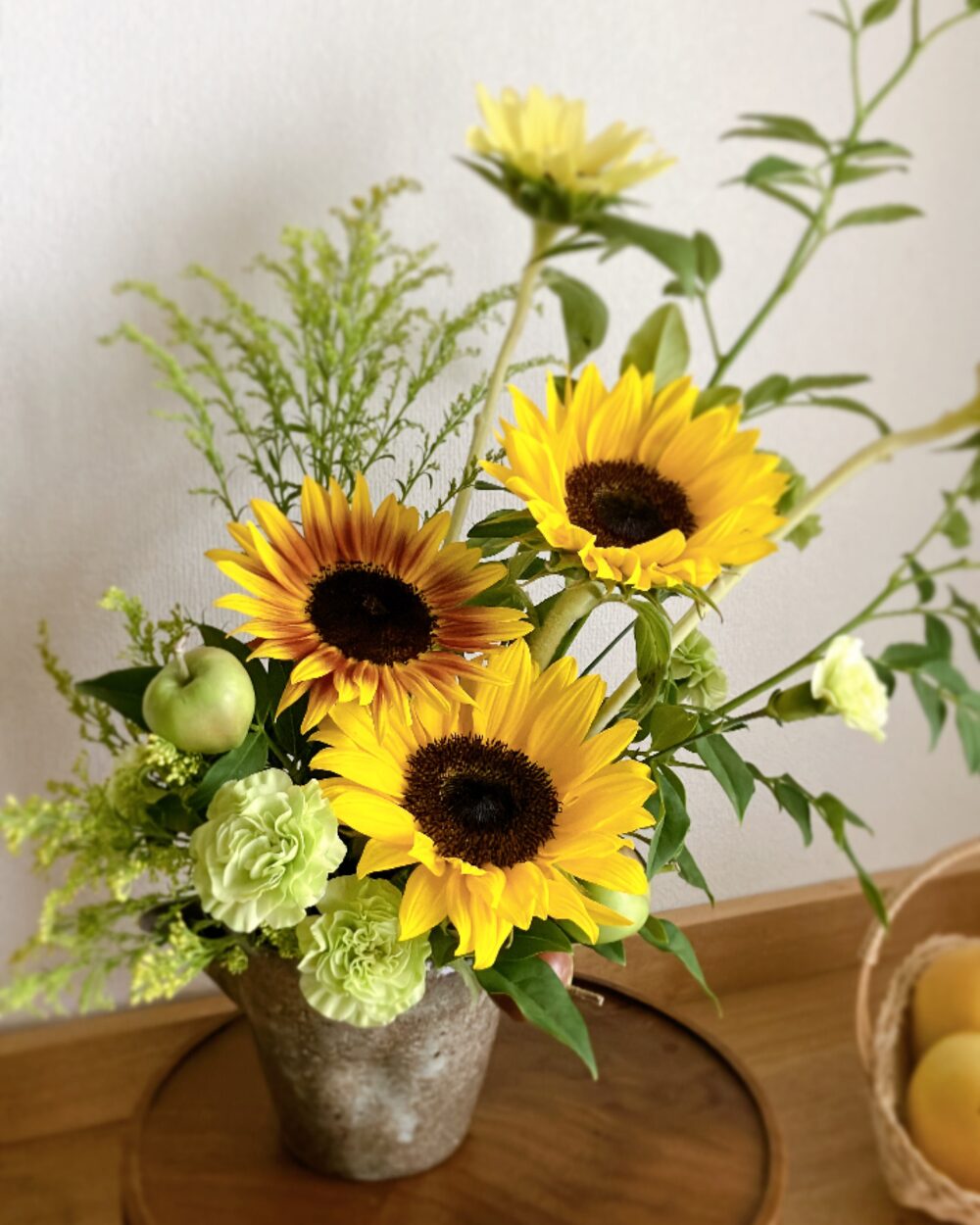 A close-up shot focusing on the contrasting textures of a bright sunflower center, soft green carnations, and tiny apples.