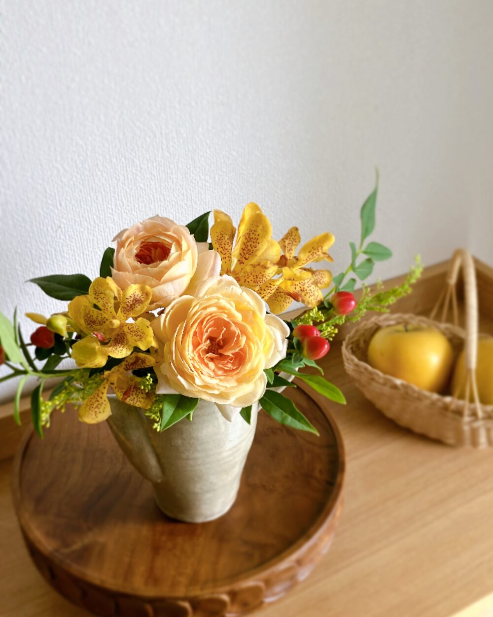A close-up of pale orange roses, yellow mokara orchids, and reddish hypericum berries showing details of the petals.