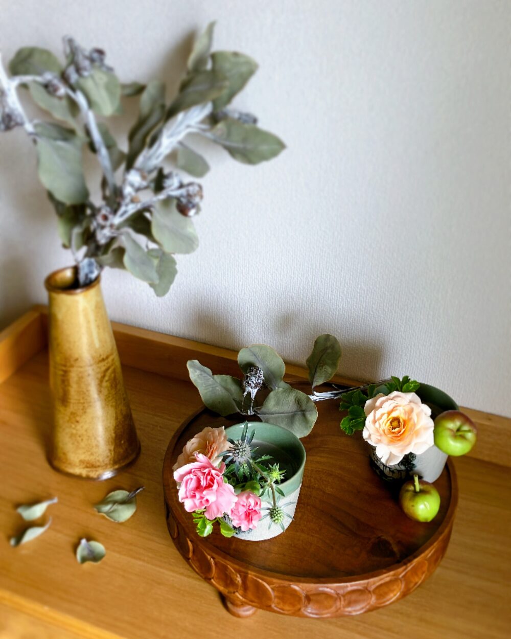 A close-up of pale orange spray roses, a pink carnation, and the rustic texture of dried tetragonanuts.