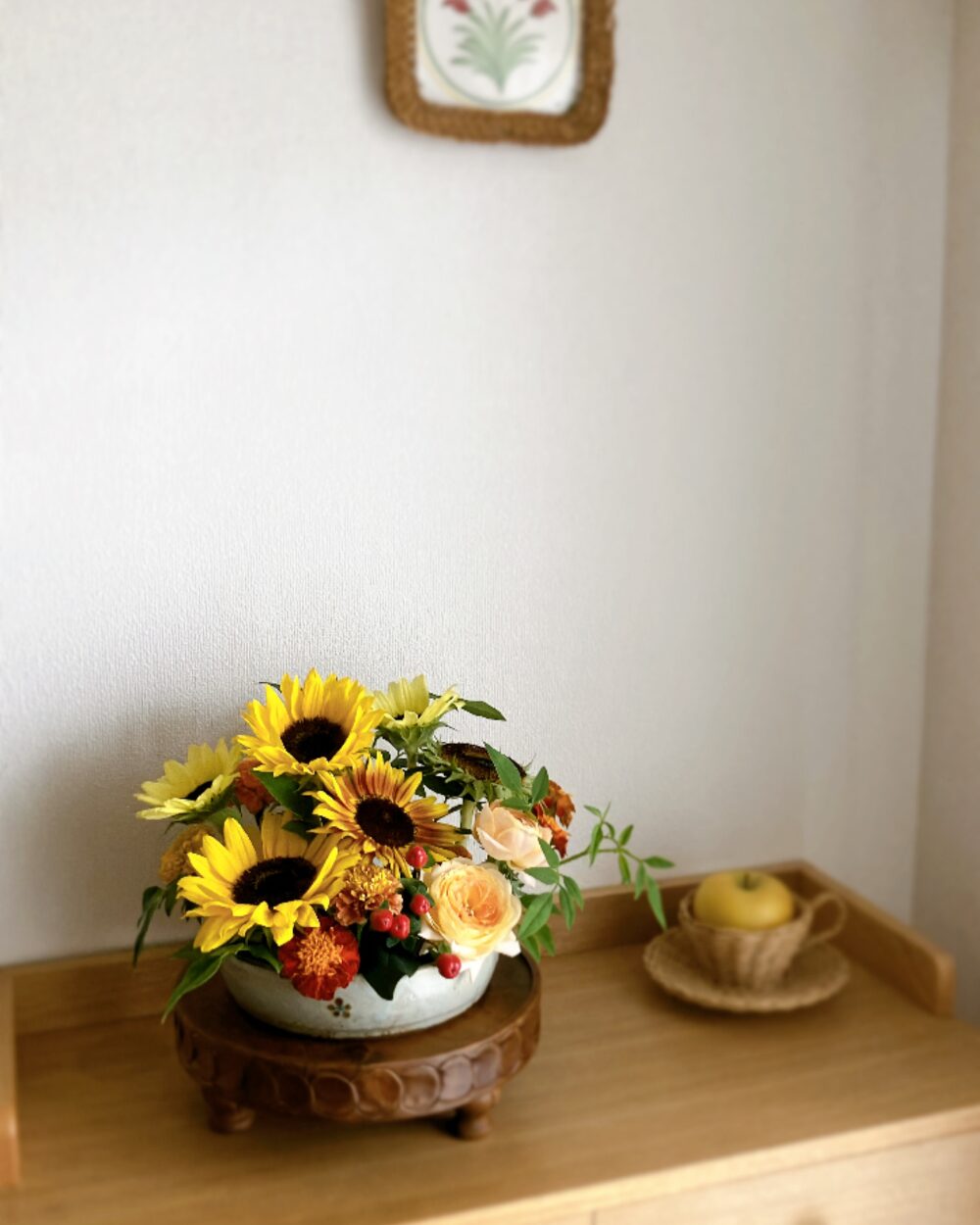 A front view of a low, densely packed arrangement combining sunflowers and freshly picked field marigolds in a flat ceramic dish.