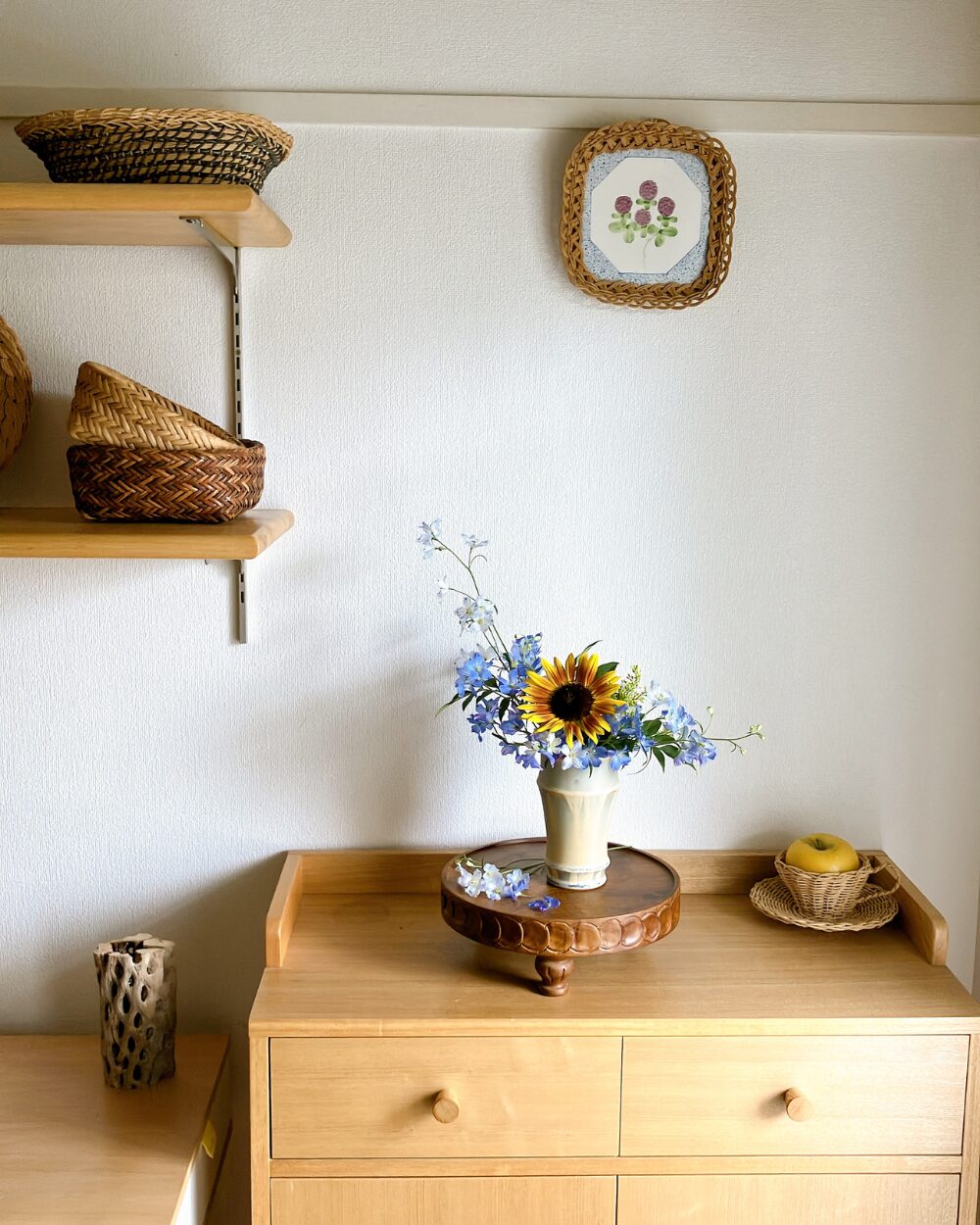 A wide view of a minimalist home interior showing a single sunflower and blue flower arrangement sitting quietly on a shelf.