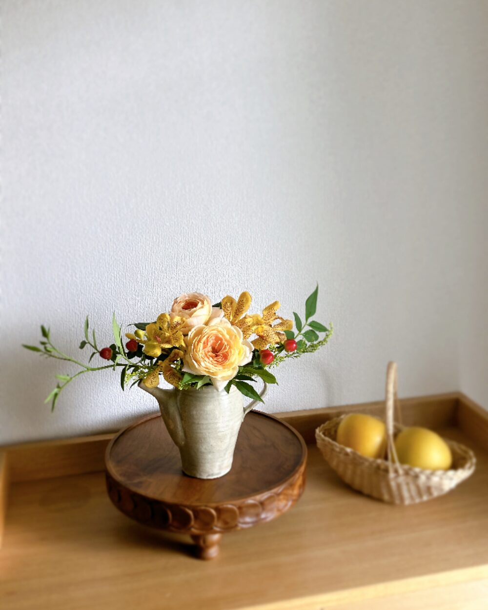 Pale orange roses and yellow mokara orchids arranged in a sleek Japanese pottery pitcher, viewed from the front.
