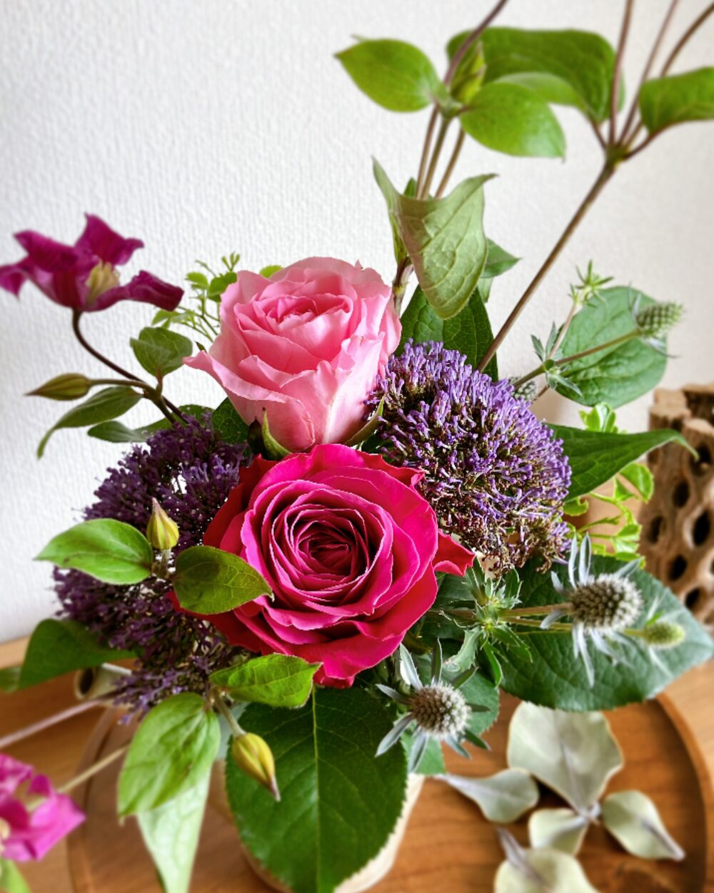 A close-up shot of deep pink and pale pink rose blossoms resting against dark purple trachelium inside a gray ceramic pitcher.