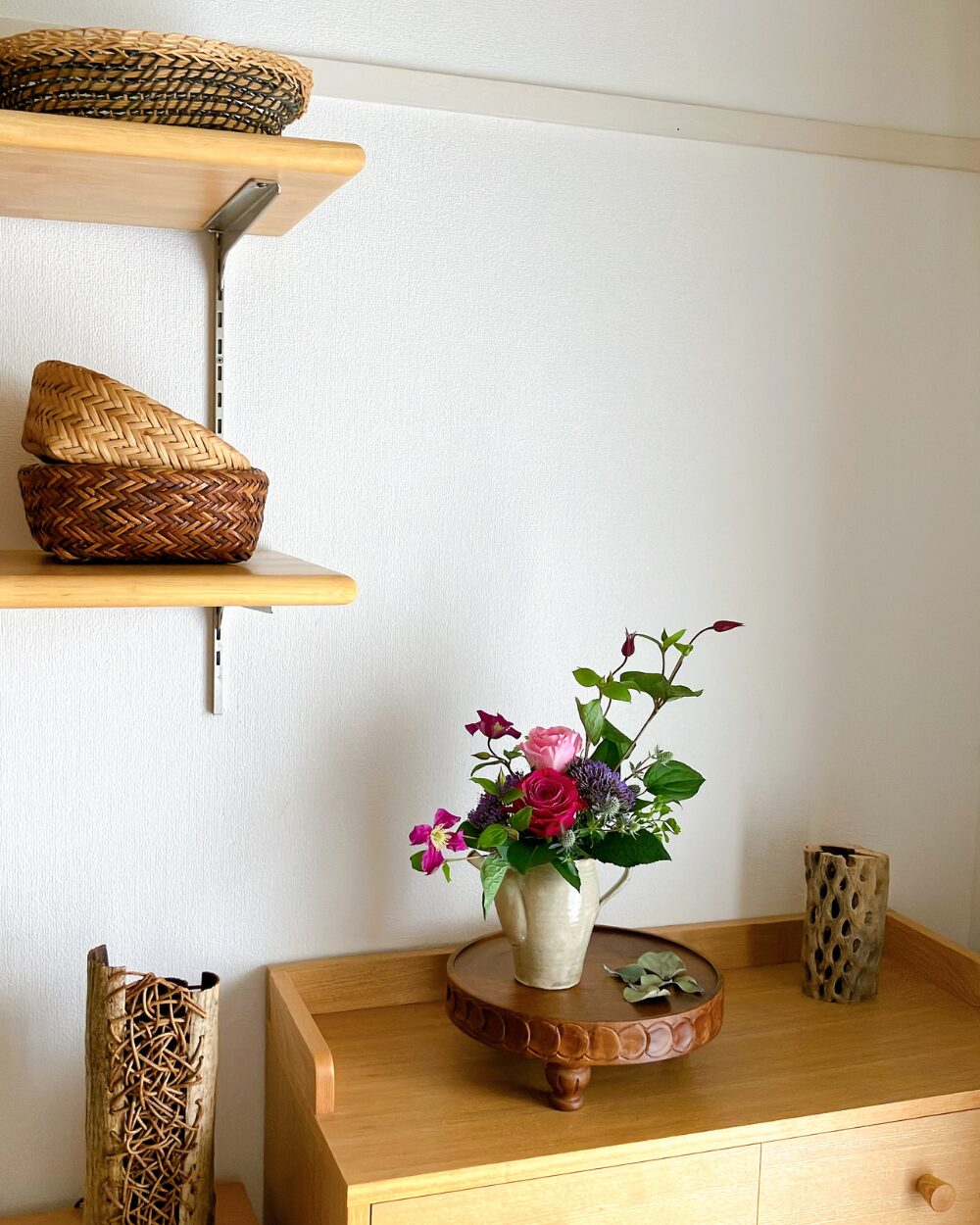 A wider view of a gray ceramic pitcher with roses and clematis displayed on a interior shelf against a dark aesthetic backdrop.