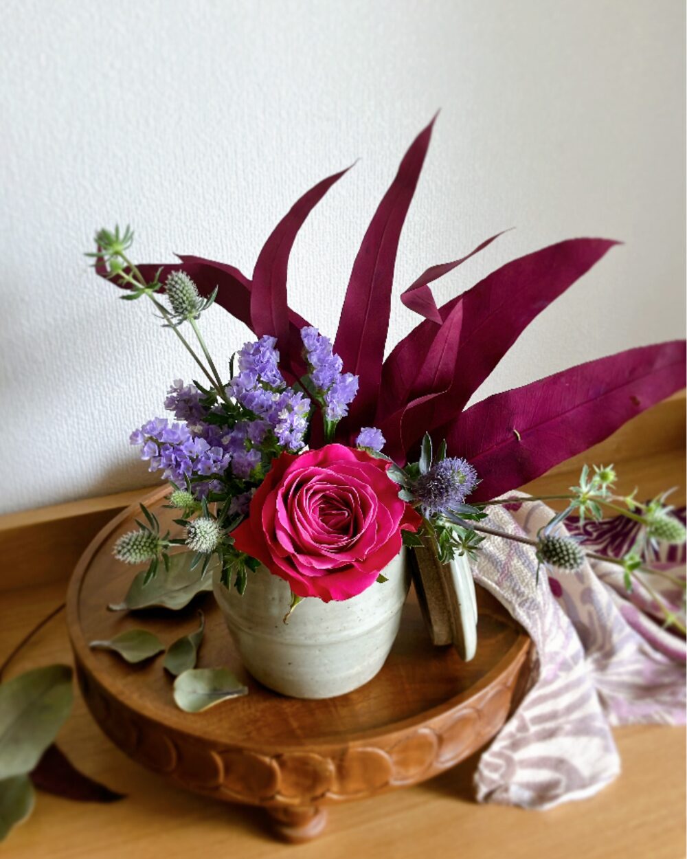 A close-up view focusing on a single deep pink rose blossom and the texture of the accompanying lidded ceramic jar.