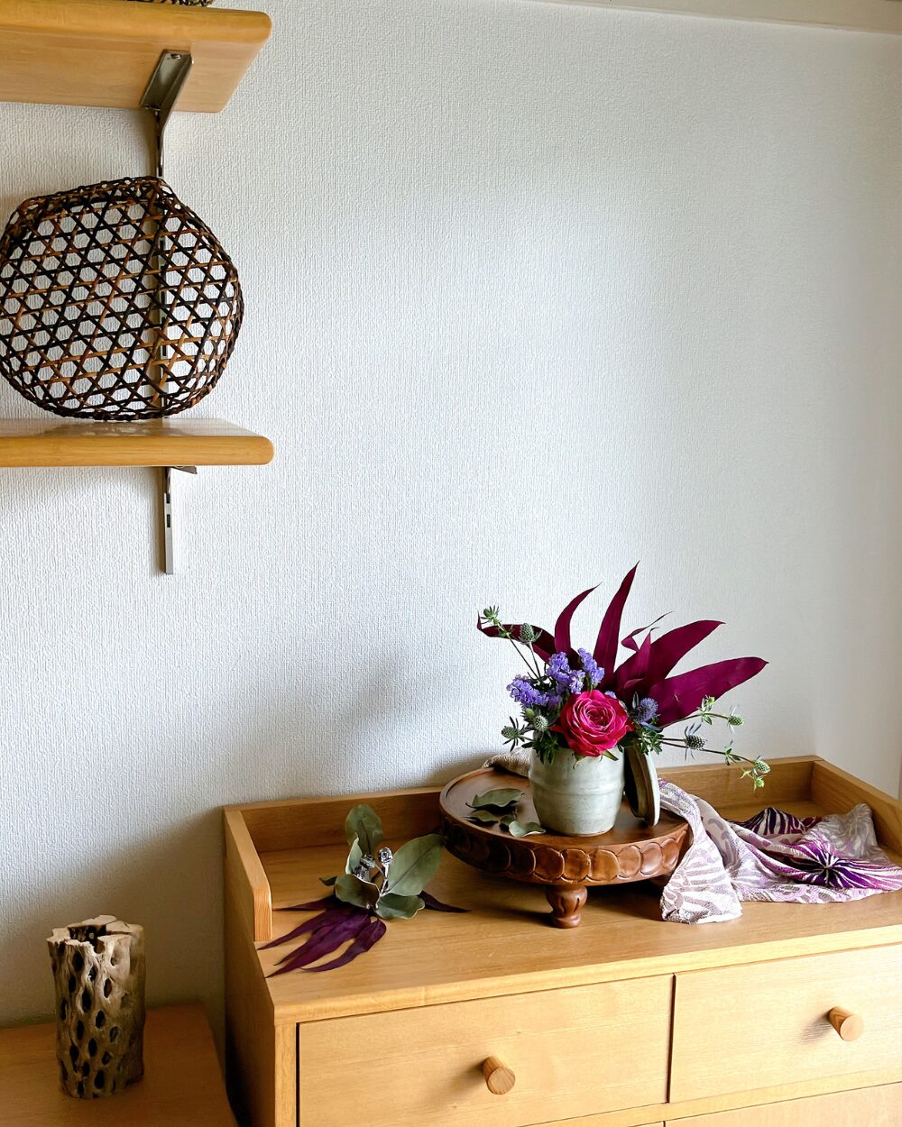 A full display shelf styled with a lidded jar arrangement, a draped gradient furoshiki cloth, dried tetragonanut clusters, and scattered eucalyptus leaves.