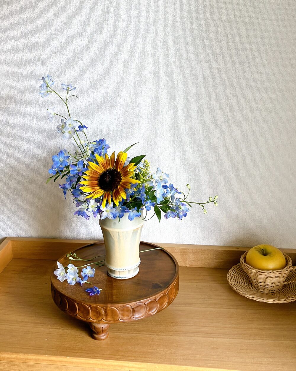 A front view of an experimental arrangement pairing a single striking sunflower with blue flowers and green foliage in a vessel.