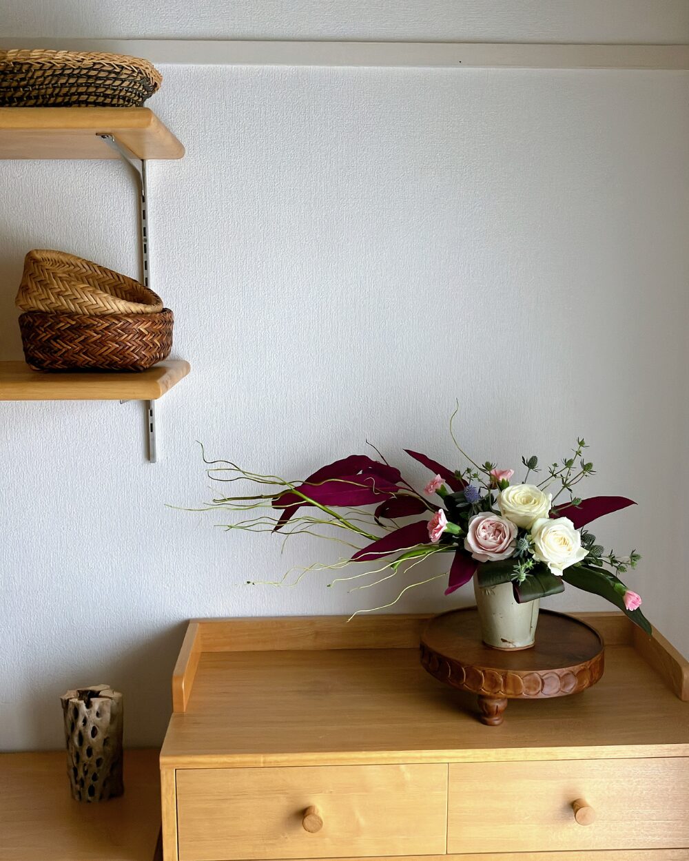 A ceramic beer cup filled with large white roses and a pale pink rose, structured horizontally with curly willow and dark pink preserved eucalyptus leaves, viewed from the front.