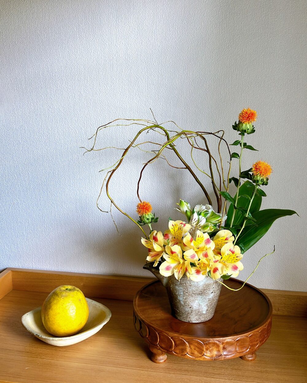 Yellow alstroemeria and safflowers with a willow arch in a deep ceramic bowl.