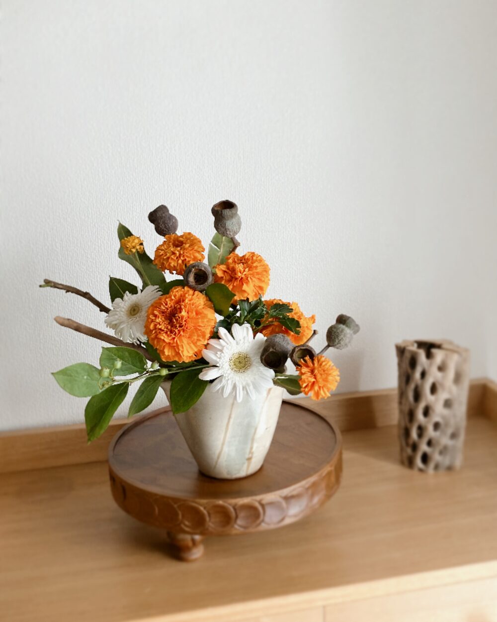 A frontal view of white gerberas, marigolds, and silver bellgum nuts arranged in a Japanese ceramic vase, with gerberas facing straight forward.