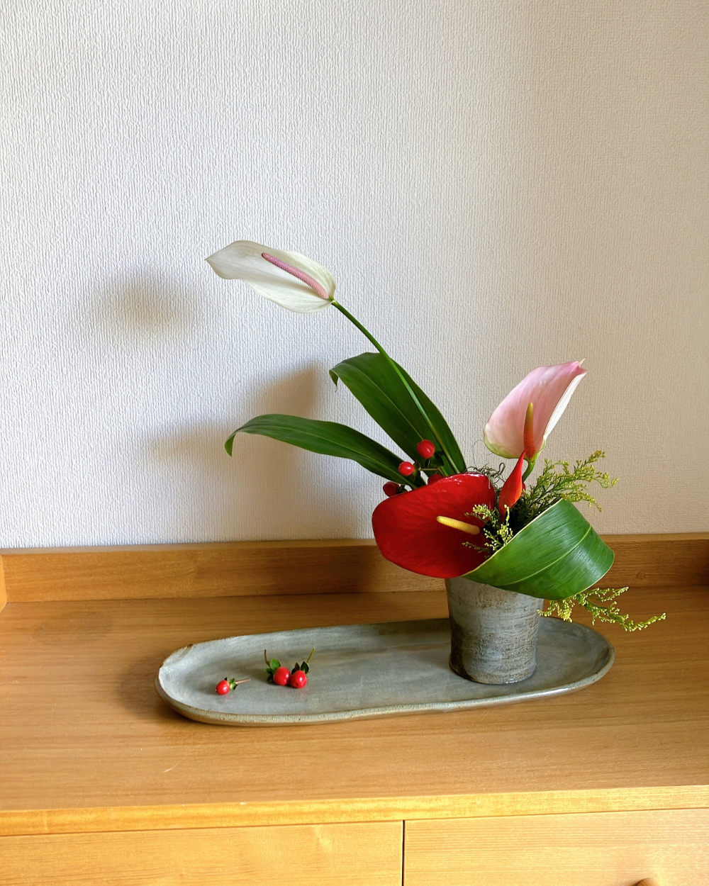 Anthurium with red berries and green foliage styled front view in a calm Japanese ceramic vessel