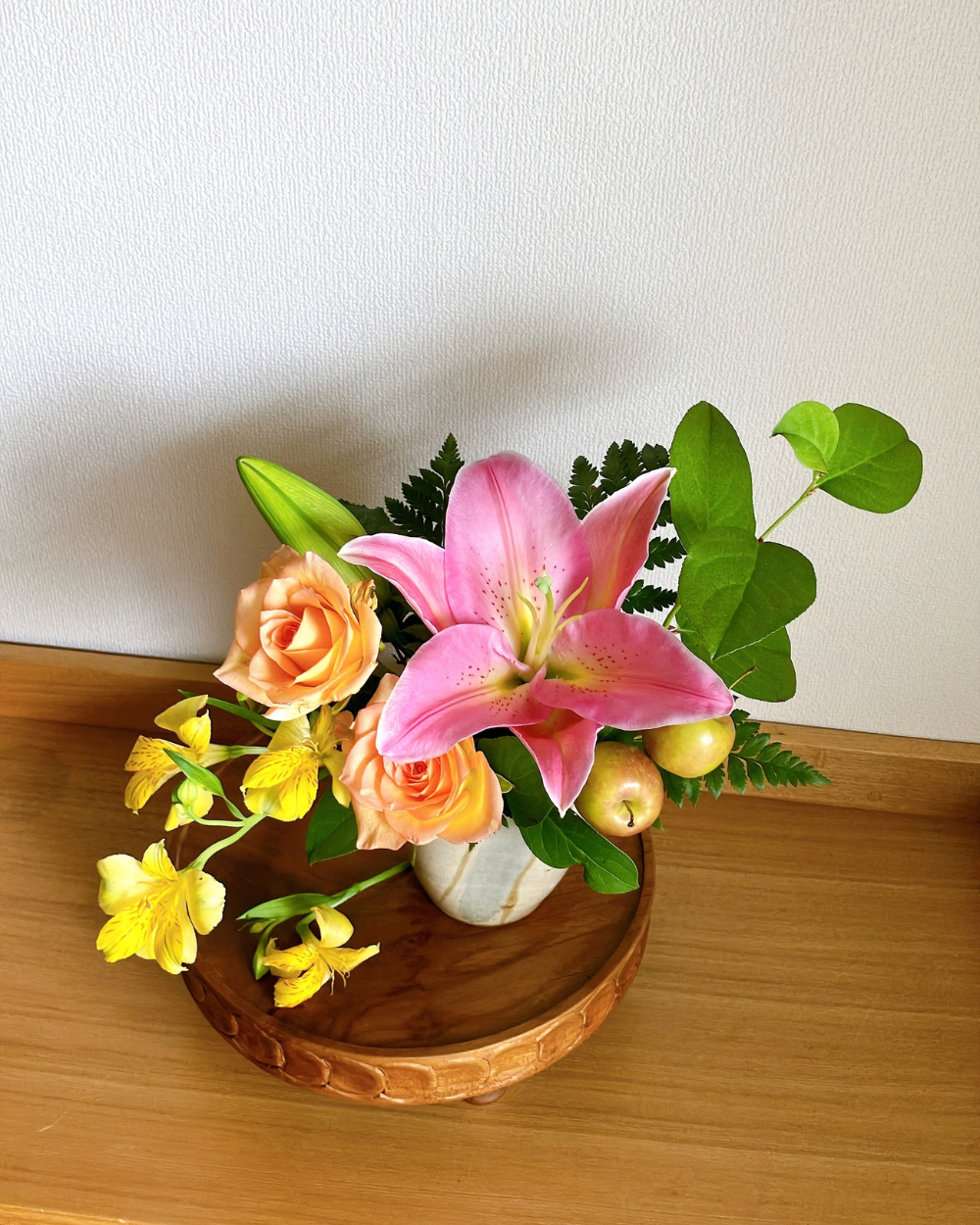 Overhead view showing the color sequence of pink lily, orange rose, and yellow alstroemeria in a ceramic cup.