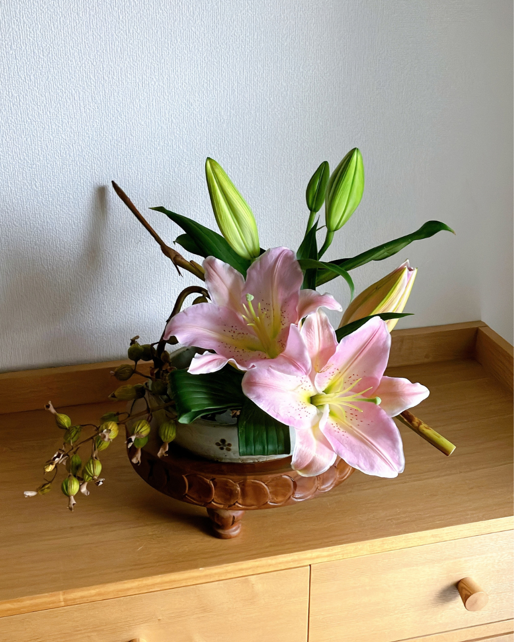 Front view of pink lily blossoms paired with angled shell ginger pods on a Japanese ceramic plate.