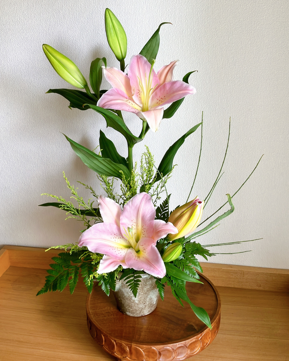Front view of two vertical pink lily blooms in a handmade Japanese pottery with green leaves.