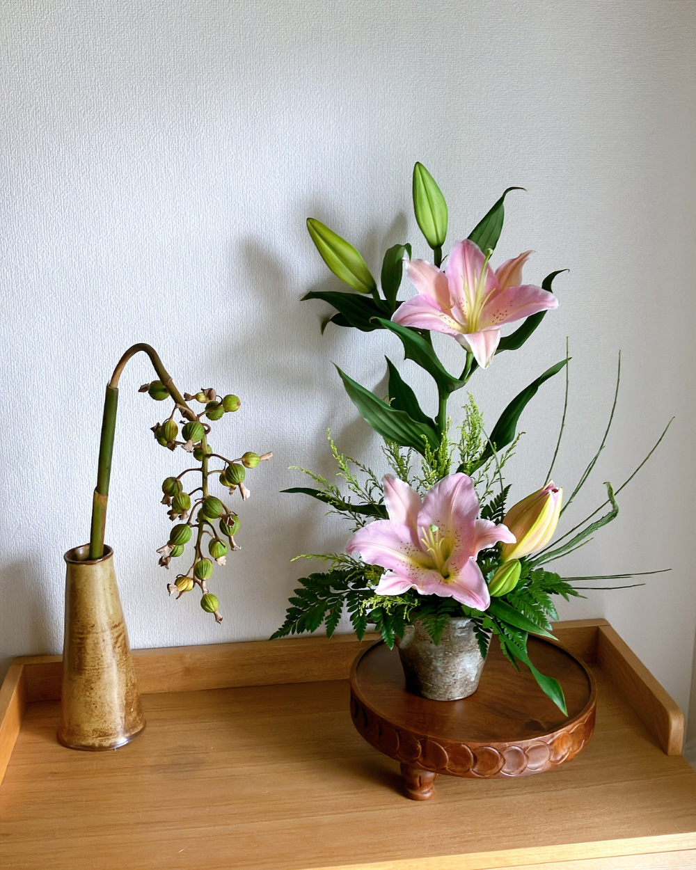Front view of two vertical pink lily blooms in a handmade Japanese pottery with Shell Ginger Pods.