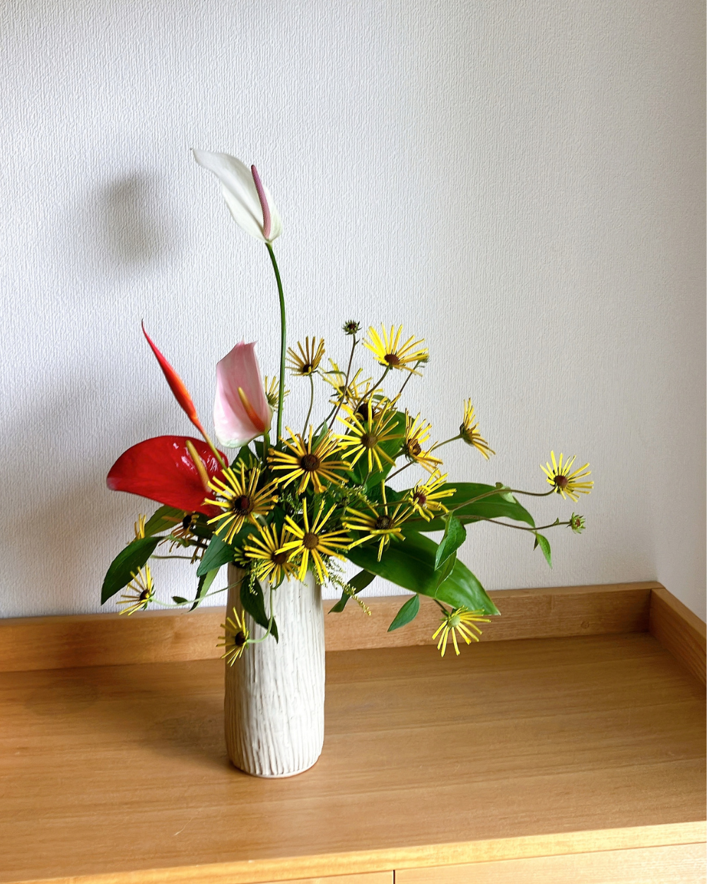 Tall Kasama ware ceramic vase styling featuring rudbeckia blooms facing forward alongside anthurium