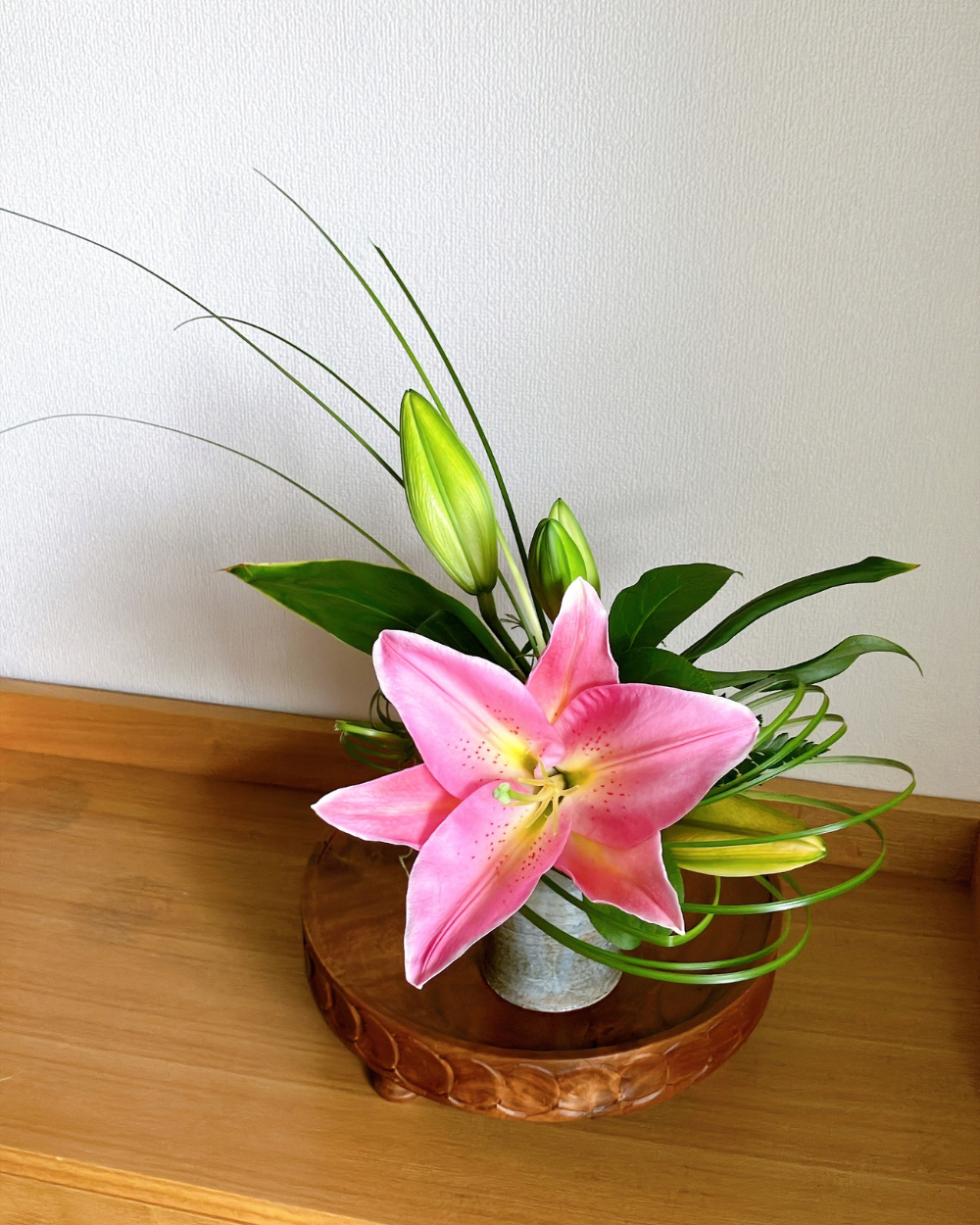 Front view of a fully opened deep pink lily blossom in a textured Shigaraki ceramic cup.