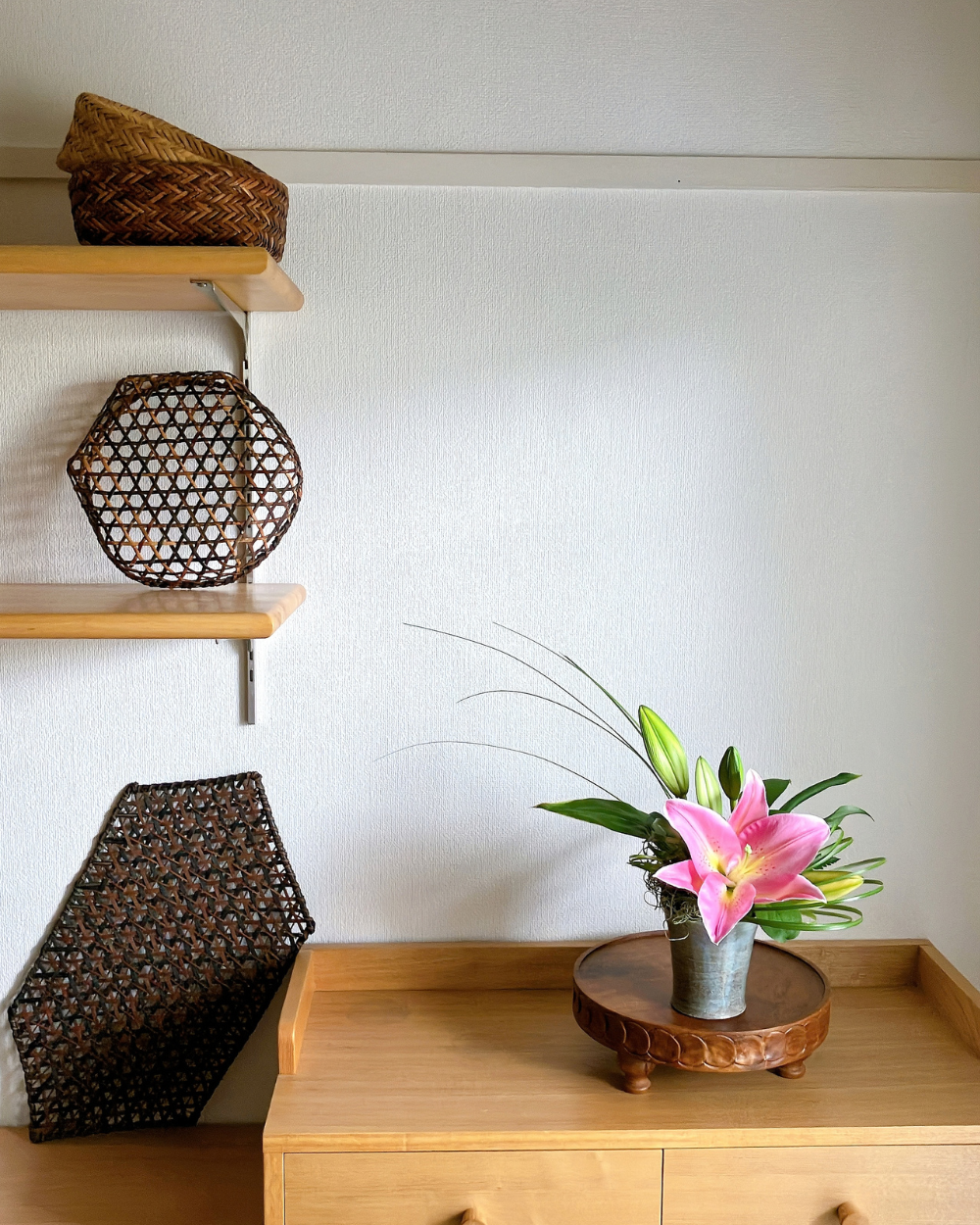 A single vibrant pink lily bloom in a Shigaraki ceramic cup placed on an interior shelf setup.